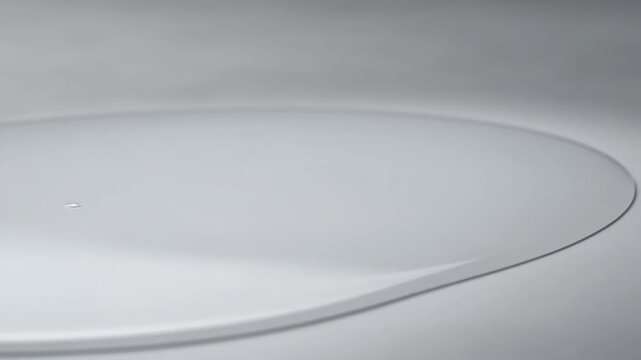 Clear cosmetic serum or hyaluronic acid in the shape of a glass stem dissolving and spreading on a clean white background, creating ripples and drops in a minimalist setting