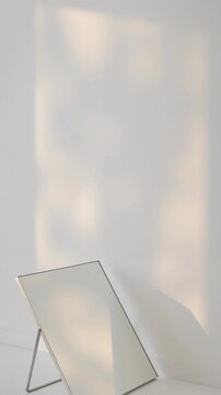Morning light and shadow moving on a white wall in a minimalist interior with a mirror, creating a beautiful, aesthetic, and calming atmosphere for a modern home