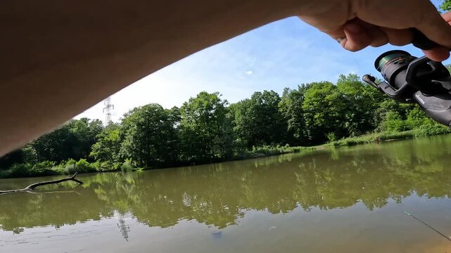 POV angler fighting a fish on a forest lake, fishing rod bent under high tension. Action shot of summer sport fishing.