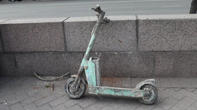 Close up of abandoned rental electric scooter covered with dirt and oxidation showing signs of long term outdoor exposure