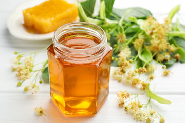 Naklejka premium Sweet honey in glass jar, honeycomb and linden flowers on white wooden table, closeup