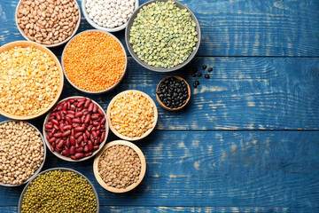 Obraz premium Different types of legumes in bowls on blue wooden table, flat lay. Space for text