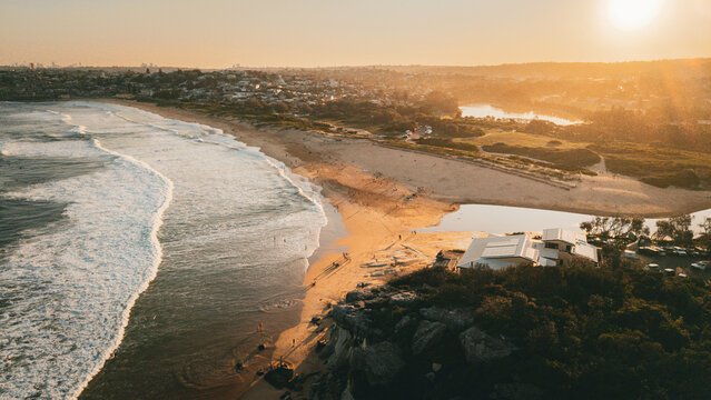 Aerial view of Curl Curl Beach at golden hour with rolling waves, sandy shoreline, and coastal vegetation in Dee Why, NSW, Australia.