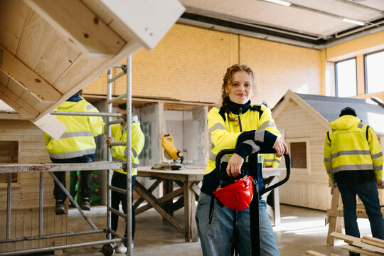Portrait of smiling young female student leaning on pallet jack while standing in training center at vocational school