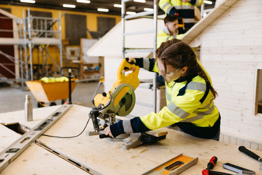 Focused young female student using miter saw wooden at workbench in vocational hub