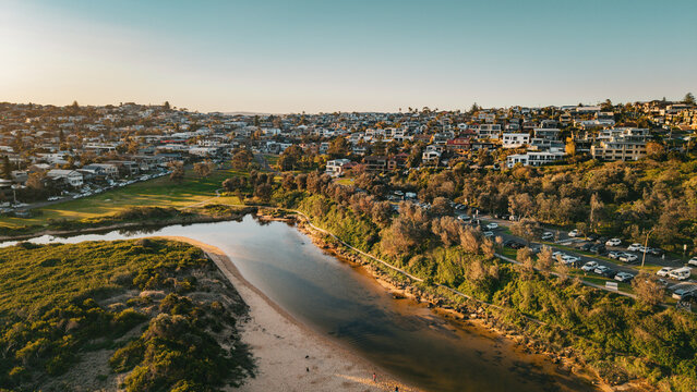 Aerial view of Curl Curl Lagoon surrounded by lush vegetation, residential houses, and a coastal parking area during golden hour in Dee Why, NSW, Australia.