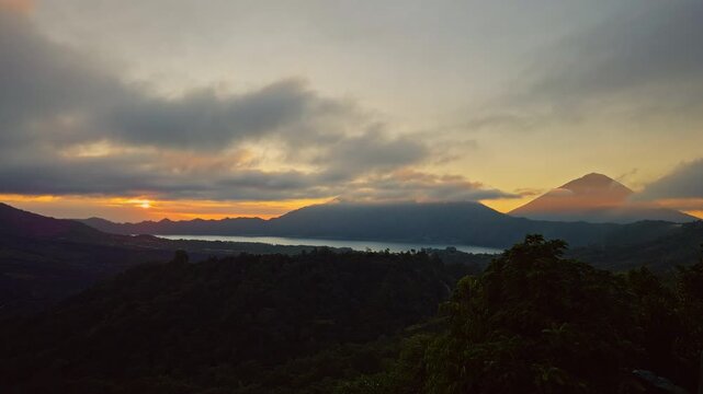 Timelapse Sunrise View of Gunung Batur and Gunung Abang With Fast Moving Clouds Above Lake and Forested Highlands Under Golden Morning Light