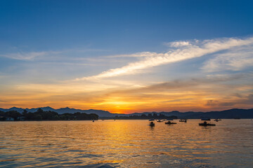 Obraz premium Sunset over calm lake with boats and mountain silhouettes