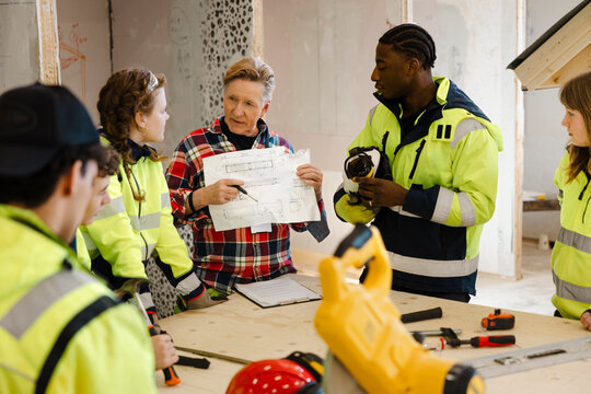 Senior male instructor showing blueprint to students while teaching civil engineering subject in vocational workshop
