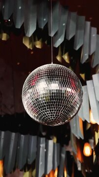 Vertical video. Close-up of hanging mirror disco ball spinning inside wedding reception tent.