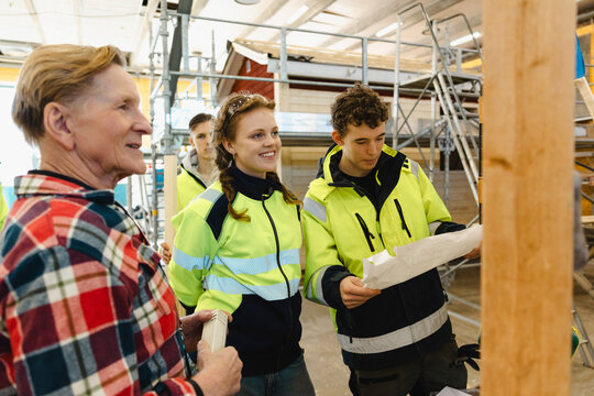 Smiling senior male instructor standing with vocational students examining blueprint during training session in high sch