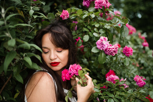 Beautiful adult woman 35-39 year old holding rose flowers with pink petals in garden close up. Natural beauty.