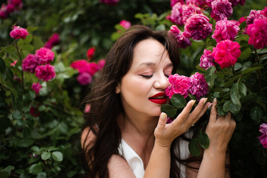 Beautiful adult woman 35-39 year old holding rose flowers with pink petals in garden close up. Natural beauty.