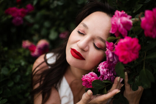 Beautiful adult woman 35-39 year old holding rose flowers with pink petals with eyes closed in garden close up. Natural beauty. Top view.