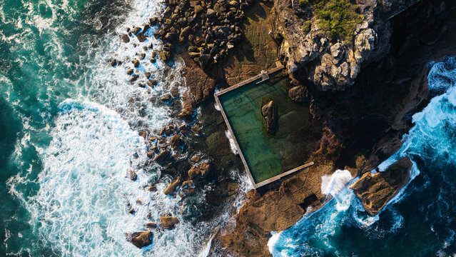 Aerial view of the Curl Curl rock pool nestled into the rugged coastline with crashing waves and turquoise water in Dee Why, NSW, Australia.