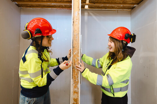 Happy female technical students enjoying with each other while standing at opposite sides of drywall panel in constructi