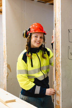 Portrait of smiling young female student wearing hardhat standing near drywall at mockup construction workshop in school