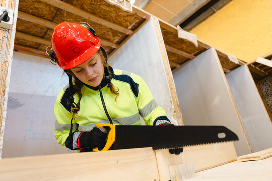 Low angle view of young female trainee cutting wooden plank with hand saw at training session in secondary school