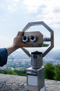 Hand of tourist adjusting public binoculars on city viewpoint
