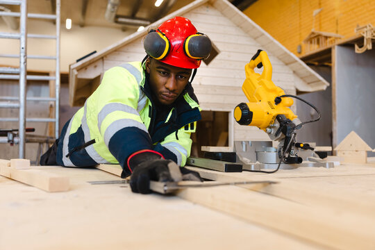 Young male vocational student leaning over wooden workbench while using framing square next to miter saw at trade school
