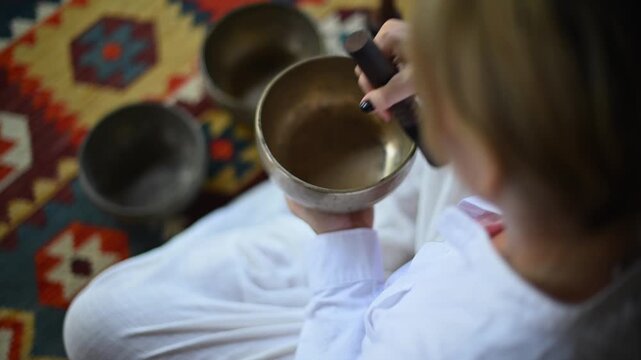 Person playing tibetan singing bowls, in patterned fabric backdrop
