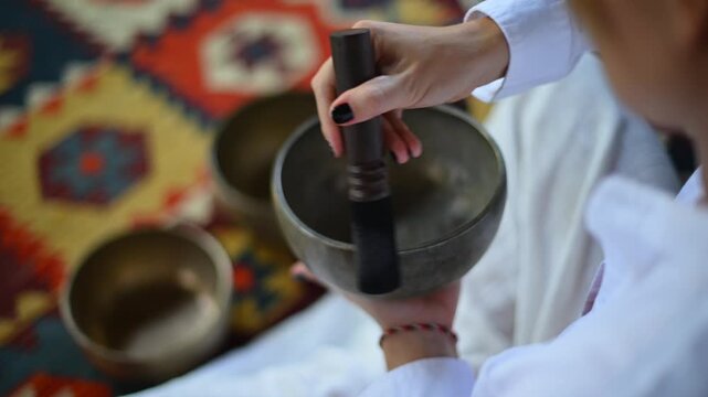 person playing striking and holding tibetan singing bowls on patterned carpet