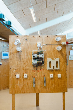 Wooden practice board with central electrical component panel and light fixtures in vocational training workshop