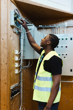 Young vocational student wearing reflective vest adjusting components inside wall mounted electrical junction box during