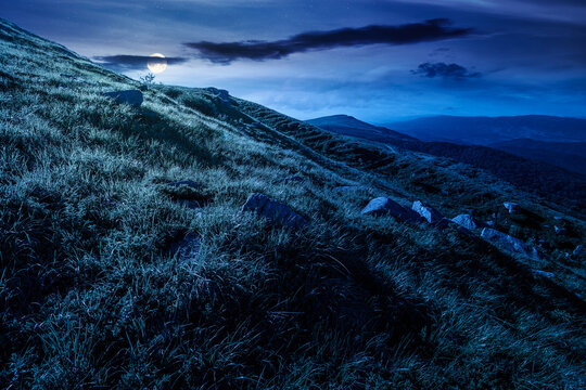 mountain landscape with grass and rock on a slope at night. mysterious view in to the distant valley of carpathian mountains. full moon over mountainous fantasy scenery of ukraine in summer
