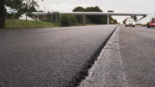 Freshly paved black asphalt road with traffic driving in the background on a new highway lane construction site