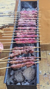 Traditional Italian arrosticini lamb skewers grilling on narrow charcoal barbecue canalina preparing delicious regional meat street food delicacy during outdoor party in Italy concept.