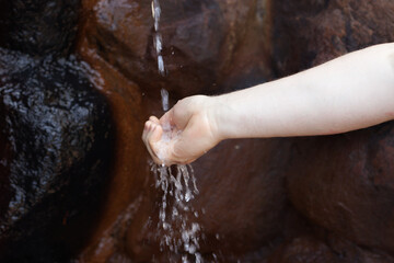 Fototapeta premium Close-up photo of a human hand catching a flowing water stream near a dark stone surface