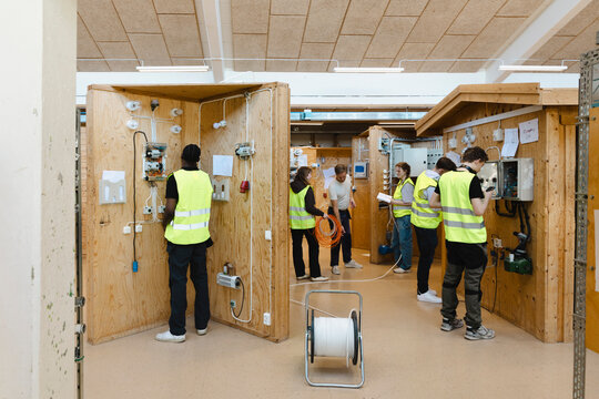 Young vocational students engaged in hands on tasks inside separate electrical training booths within large instructiona