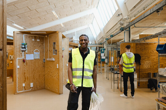 Portrait of smiling young male student holding bundle of white wiring while standing in training center at vocational se