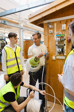 Experienced instructor demonstrating technical wiring techniques to young students in vocational workshop