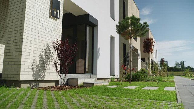 Modern residential townhouse complex exterior with manicured lawn and eco-friendly permeable paving on a sunny day representing contemporary suburban living and real estate