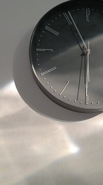 Modern circular  gray or black clock against a white wall with sun reflections. Capturing the passage of time. 4K vertical video.