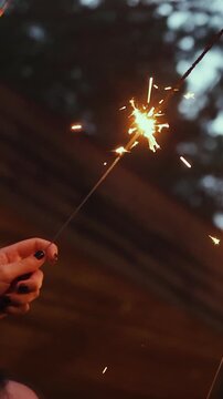 Vertical video. Hand holding burning sparkler during outdoor wedding celebration at night.
