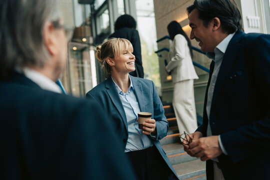 Smiling businesswoman talking with male colleagues near stairs in office building
