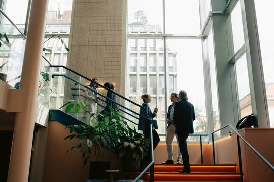 Business professionals talking with each other while standing on stairs in office building