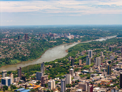 Aerial view of the Parana River winding through the urban landscape, featuring modern high-rise buildings and dense green vegetation in Foz do Iguacu, State of Parana, Brazil.