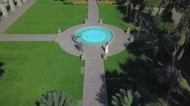 Aerial Drone Shot of Bride and Groom Walking Through Elegant Garden with Fountain at Luxury Wedding Venue