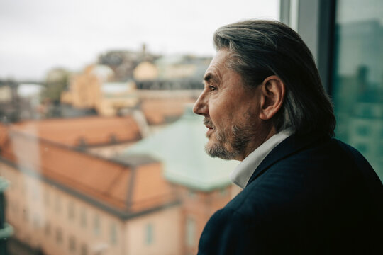 Contemplative senior businessman looking out through window in office