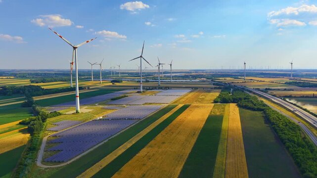 Wind turbine over colorful striped agricultural fields. Aerial view of turbine beside purple, green and brown striped farmland rows, sunny sky