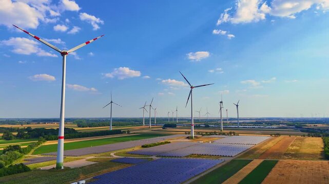 Wind turbine close up above green agricultural fields. Drone shot of turbine blades close up over patchwork farmland, additional turbines distant