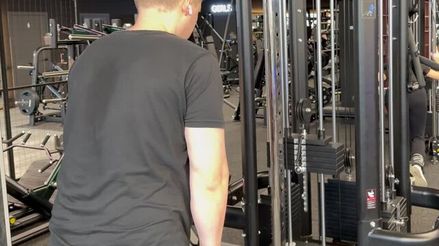 A man prepares a cable weight machine for resistance training during a focused workout session in a fully equipped fitness center
