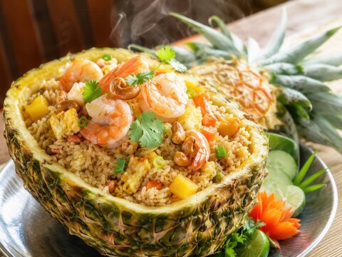 Gebratener Thai-Reis mit Garnelen, Ananas, Cashewkernen, Ei und frischem Koriander, dekorativ in einer ausgeh&ouml;hlten Ananas als exotisches Hauptgericht serviert.