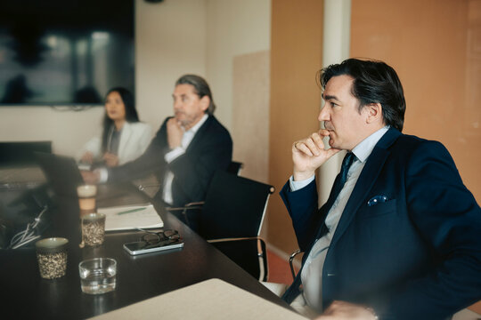 Focused male business professional sitting with hand on chin in meeting at office