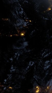 This shows a view of Earth at night from space. The image highlights the lights of cities and towns against a dark background. Clouds and natural features are also visible.