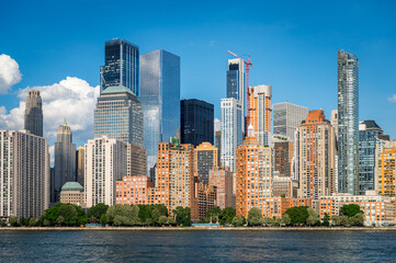 Fototapeta premium Skyline of Battery Park City buildings in New York. Horizontal waterfront shot of high rise towers and green park trees.